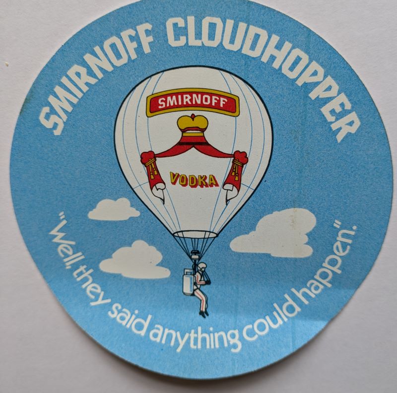 Light blue circular sticker with the Smirnoff Cloudhopper balloon drawn on it and clouds and text in white